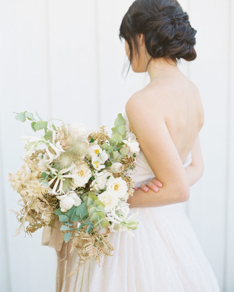 A bride with her back to the camera holding a lush bridal bouquet.Must-have wedding photos by Marcela Plosker, a Boston wedding photographer.