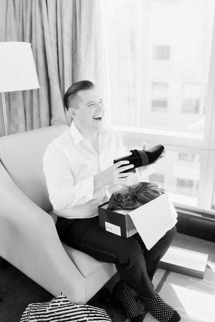 A man laughs as he puts on his shoes on his wedding day. Must-have wedding photos by Marcela Plosker, a Boston wedding photographer.