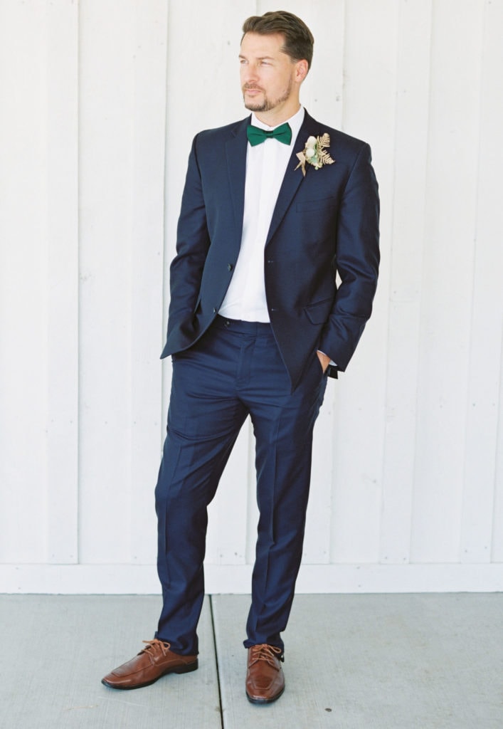 A portrait of a groom staring into the distance on his wedding day wearing a bowtie, boutonniere, and blue suit. Must-have wedding photos by Marcela Plosker, a Boston wedding photographer.