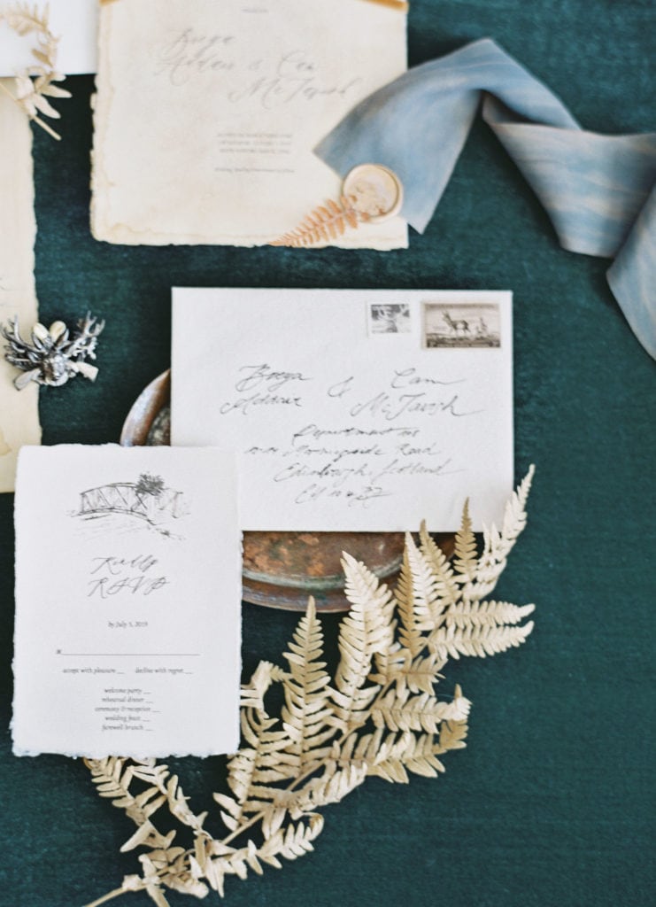 A wedding invitation suite, comprised of a couple's wedding invitations, a sprig of dried greenery, and ribbon. Must-have wedding photos by Marcela Plosker, a Boston wedding photographer.