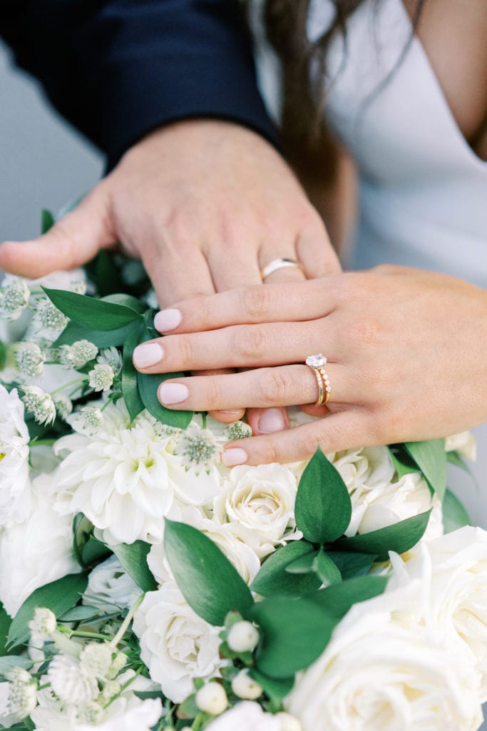 Close up image of a bride and groom overlaying their hands on the wedding bouquet as an example of a shot from a wedding photography shot list.