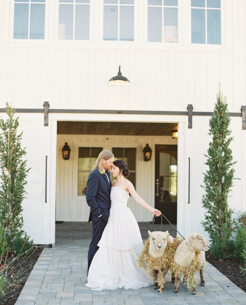 Bride and groom pose with two sheep in front of an elegant white vintage house