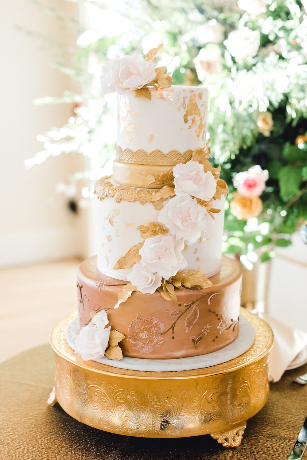 Three-tier wedding cake with gold and white theme and floral decor, taken by Marcela Diaz Photography