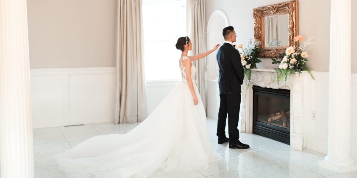 a bride taps her groom on the shoulder as he anticipates their first look while standing inside a stately room in Boston, Massachusetts