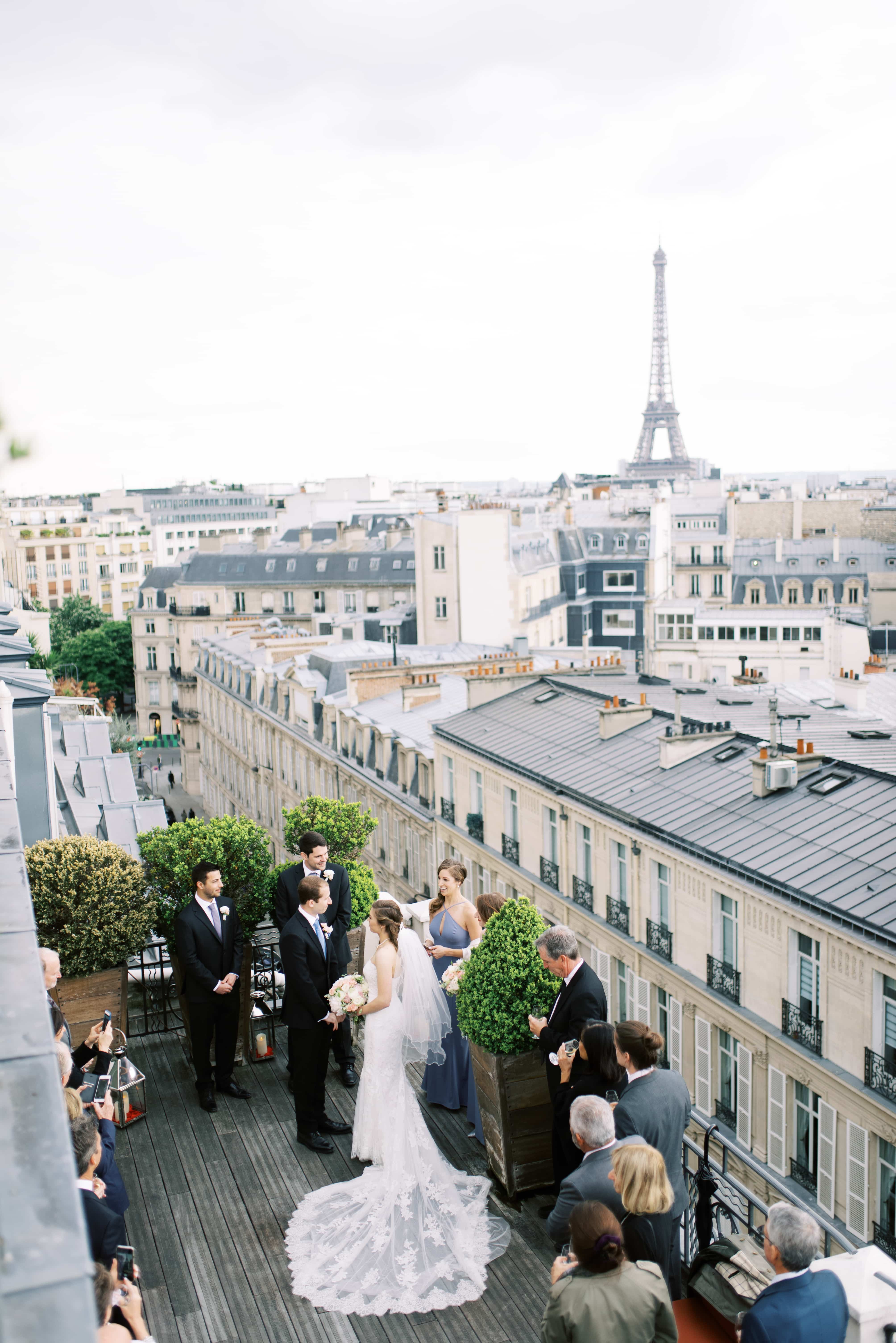 A wedding ceremony is taking place on a balcony in Paris, France, overlooking the Eiffel Tower, Photographed by North Shore, Massachusetts wedding photographer Marcela Plosker 
