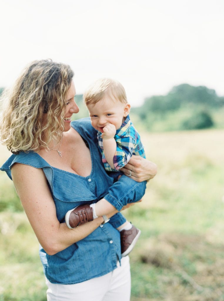 A momprenuer holds her son outside in the grass. Photographed by North Shore, Massachusetts wedding photographer Marcela Plosker