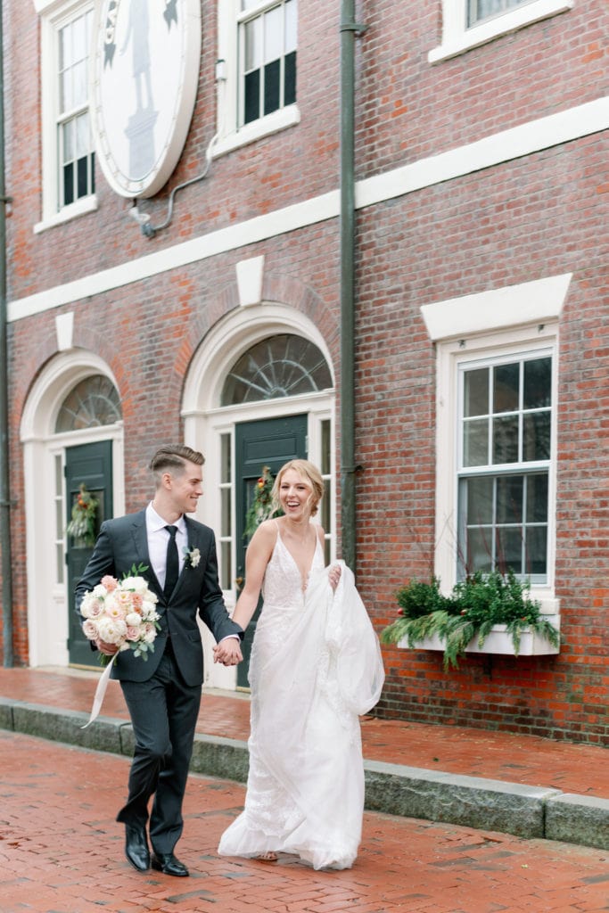 A bride and groom walk and hold hands, laughing and smiling on their wedding day. Photographed by Marcela Plosker, a Boston wedding photographer.