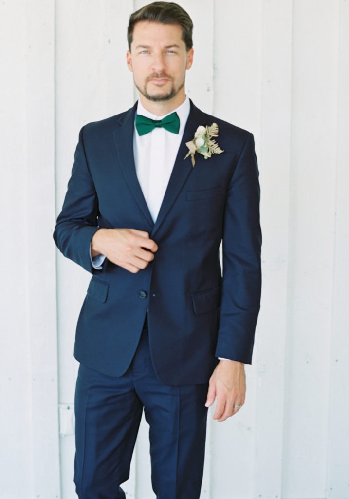 A portrait of a groom on his wedding day wearing a bowtie, boutonniere, and blue suit. Must-have wedding photos by Marcela Plosker, a Boston wedding photographer.