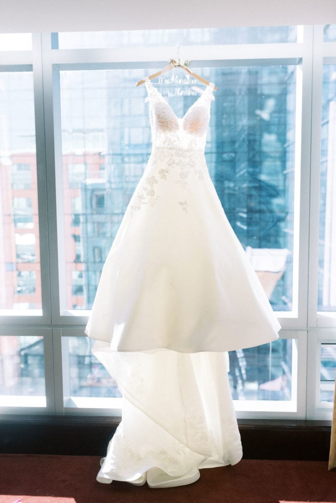 A wedding dress hangs over a floor-to-ceiling window. Must-have wedding photos by Marcela Plosker, a Boston wedding photographer.