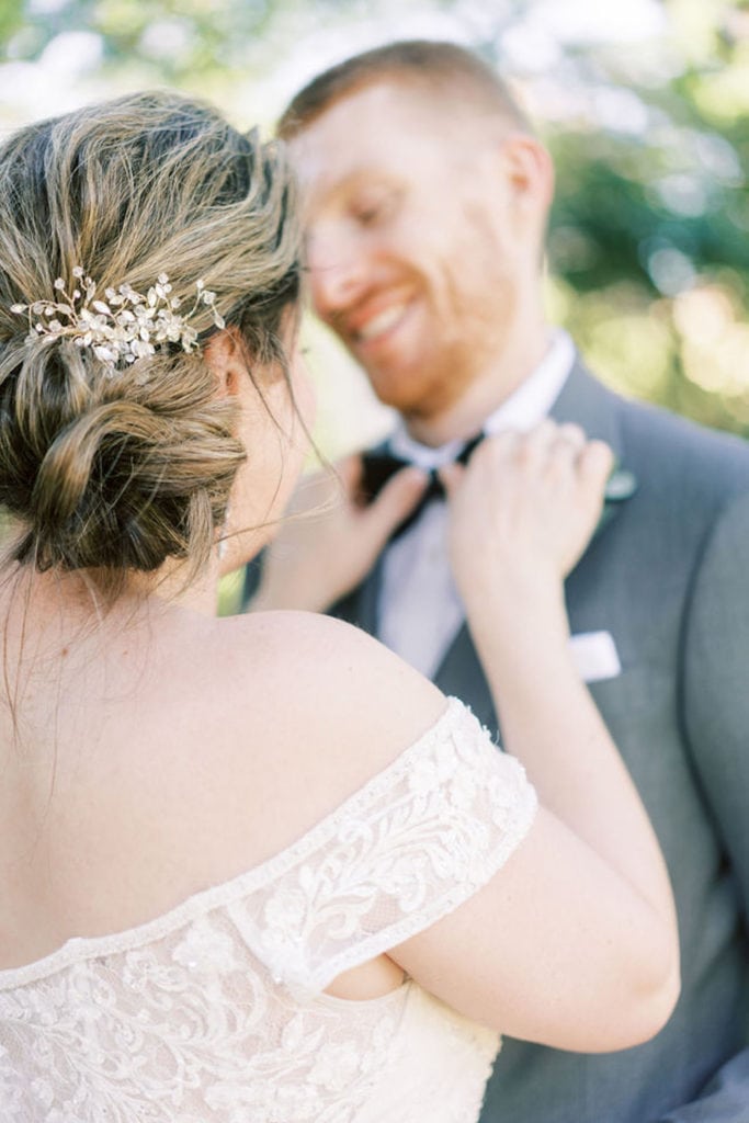 Close up of side of bride and her hairstyle as she adjusts grooms tie while he smiles about their elopement. Photograph by Northshore, Massachusetts and Boston wedding photographer Marcela Plosker.