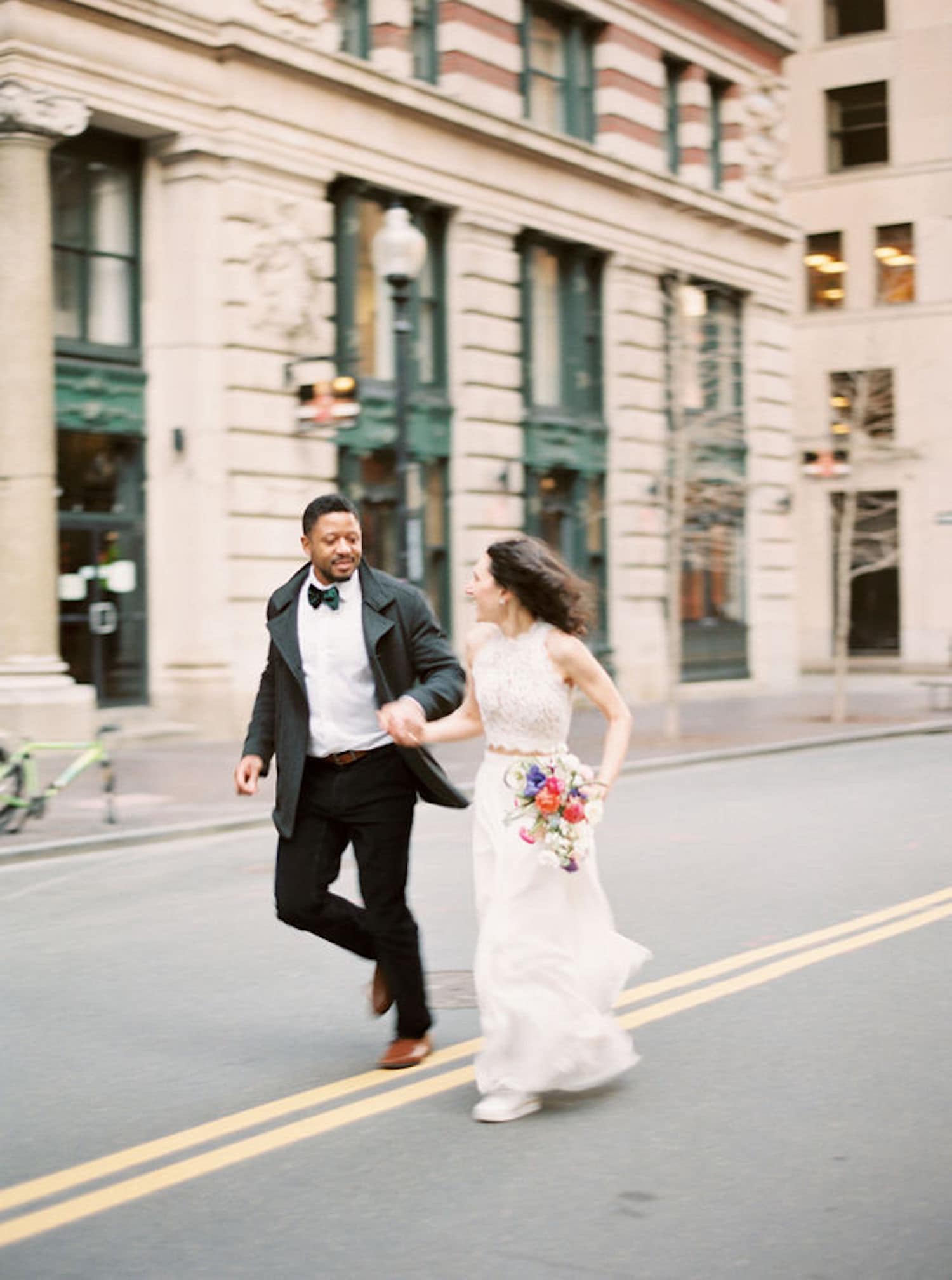 A newlywed couple holds hands as they run down the street in Boston, Massachusetts for their elopement. Photograph by Northshore, Massachusetts and Boston wedding photographer Marcela Plosker.