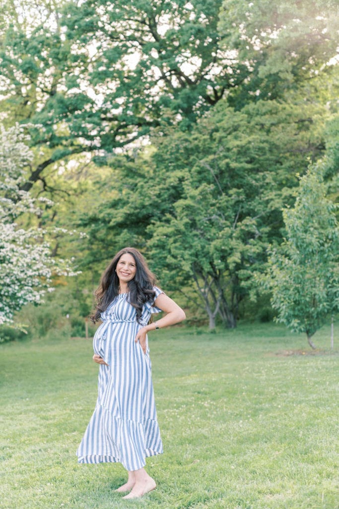 A pregnant woman smiles while embracing her belly and standing in her yard as she prepares experience The Benefits of Outsourcing as a Mompreneur.