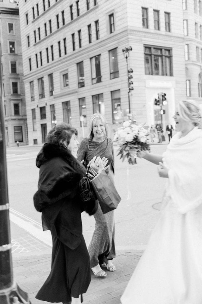 Black and white candid photo of bride with her grandmother and female wedding guest on the streets of Boston as an example of family wedding photos and how to do them right. Photograph by Boston, Massachusetts wedding photographer Marcela Plosker.