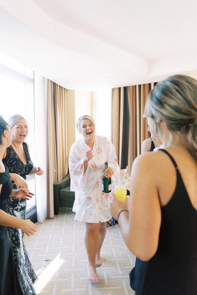 A bride and her bridesmaid laugh during their group get ready, a popular wedding tradition. Image by Marcela Plosker, a Massachusetts wedding photographer.