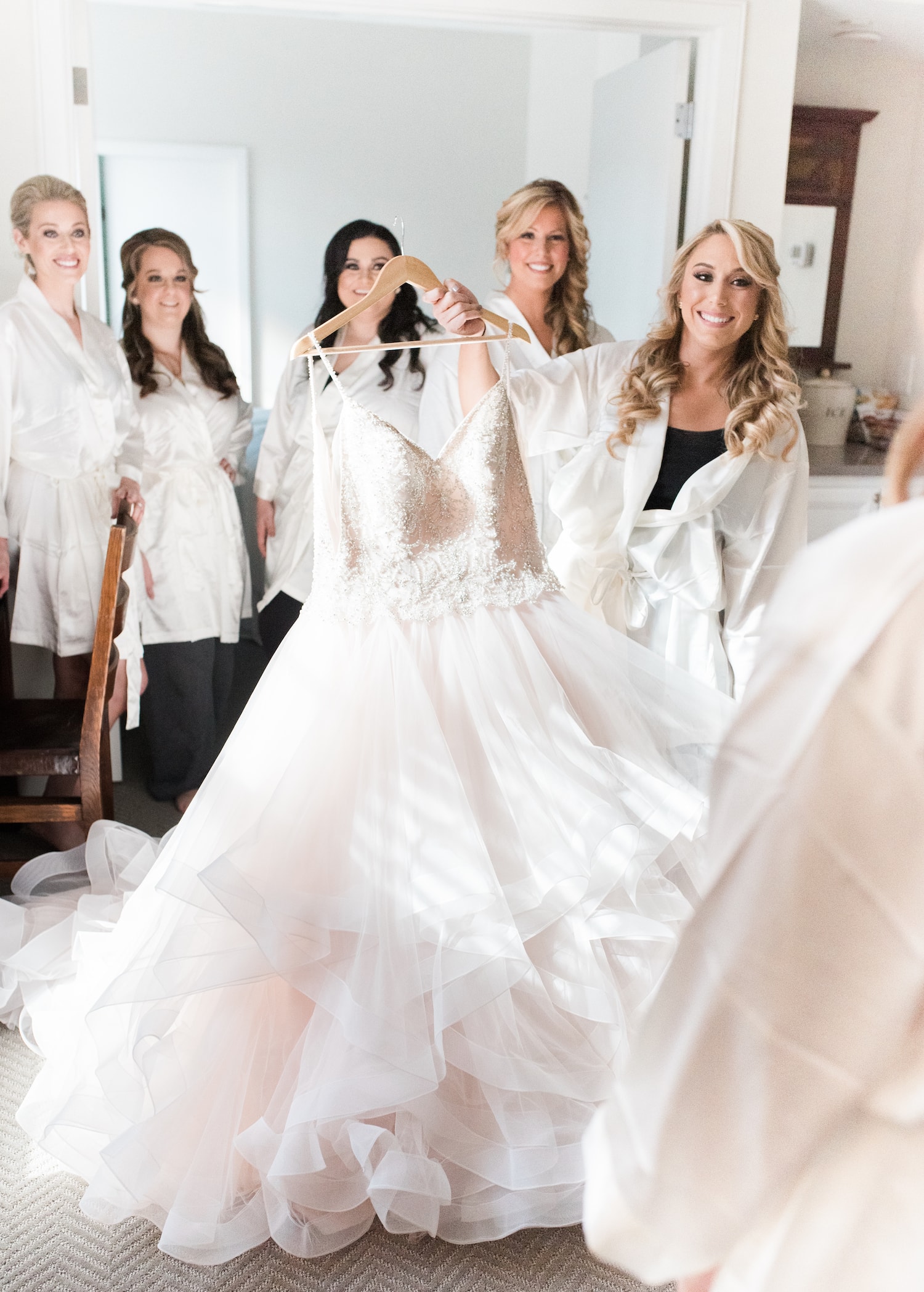 A bride holds up her dress during a group get-ready, a popular wedding tradition. Image by Massachusetts wedding photographer Marcela Plosker.