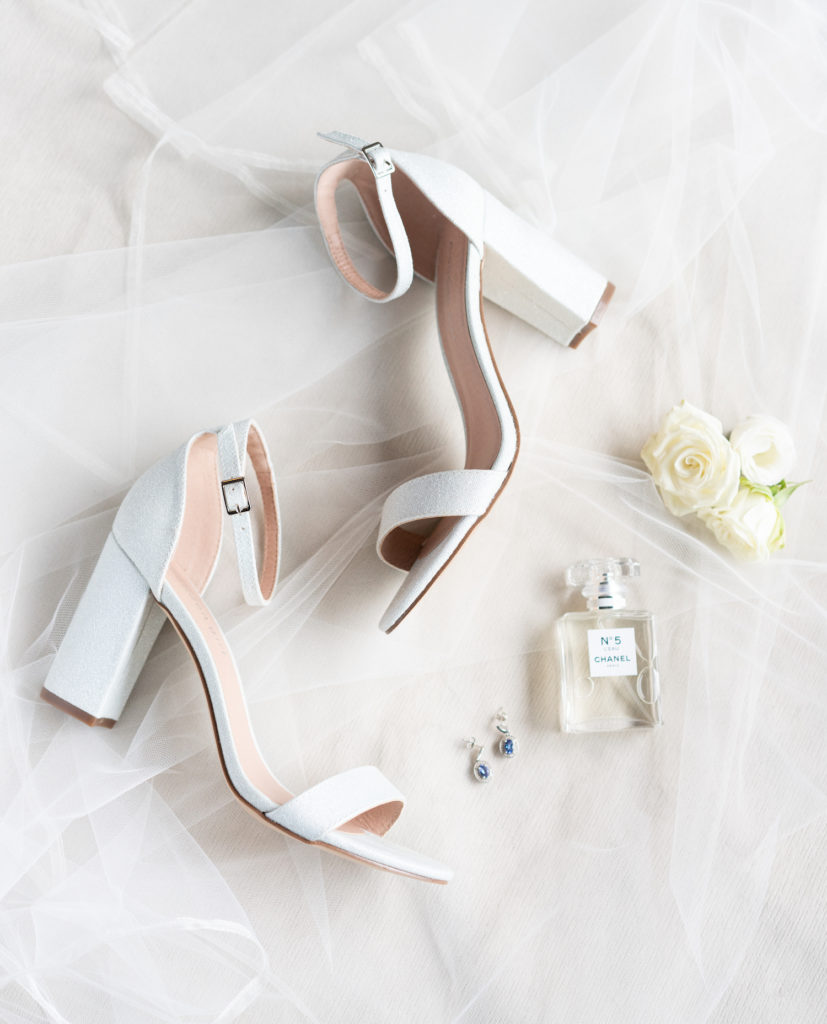 Image of bride's wedding shoes with her perfume, jewelry, and wedding flowers photographed by Marcela Plosker, wedding photographer.