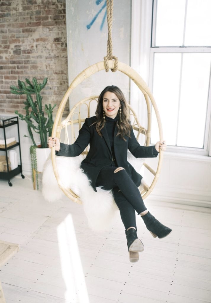How Much Do Wedding Photographers Make (2021). Marcela Diaz smiles as she sits on a wooden hanging chair