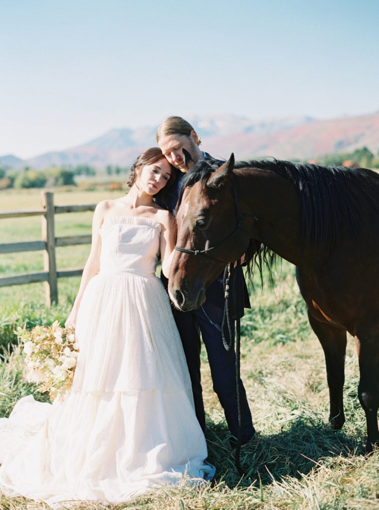 Bride and groom pose with a horse during their wedding photoshoot at a farm