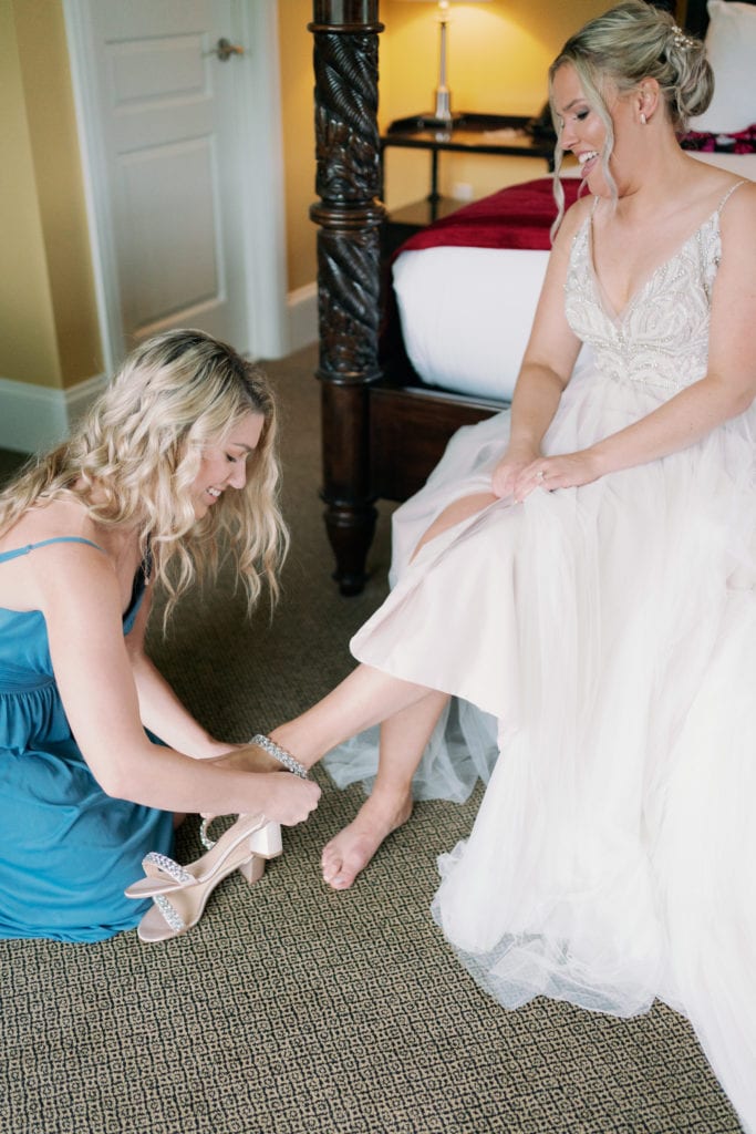 Bride gets help from her bridesmaid in putting on her bridal shoes while preparing for the wedding ceremony at Emerson Inn, Cape Ann