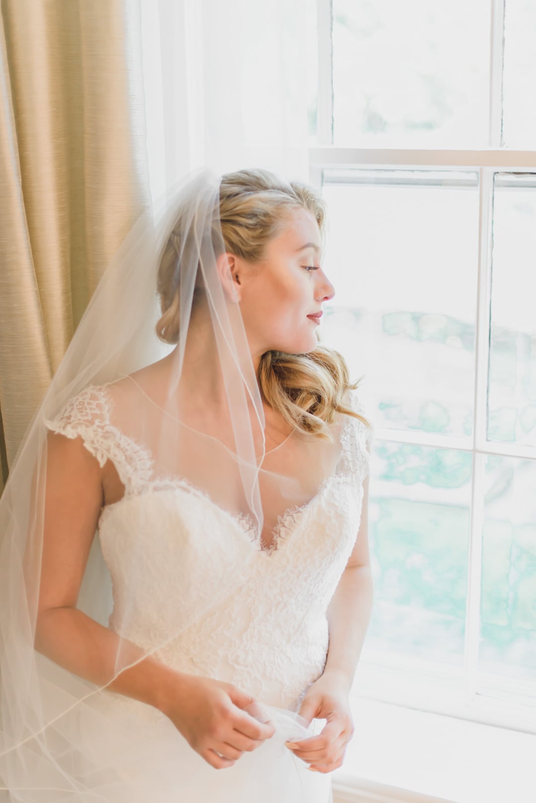 Bride looking elegant in her bridal dress as she looks out of the window in her suite at the 2101 Commonwealth in Boston