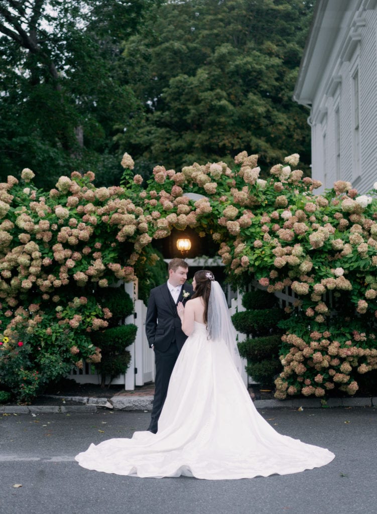 Bride and groom stand close to each other with flowers in bloom behind them, shot by Marcela Diaz