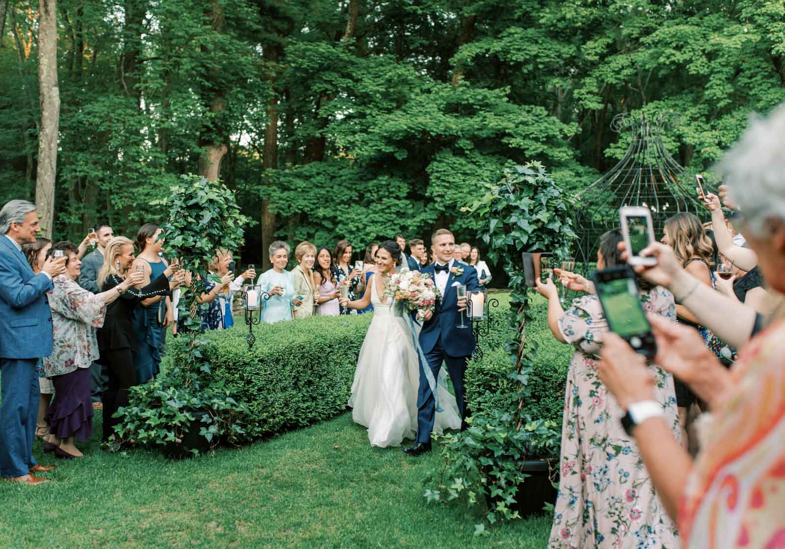Bride and groom walking out of their wedding ceremony in Vermont with their wedding guests applauding and taking photos of them