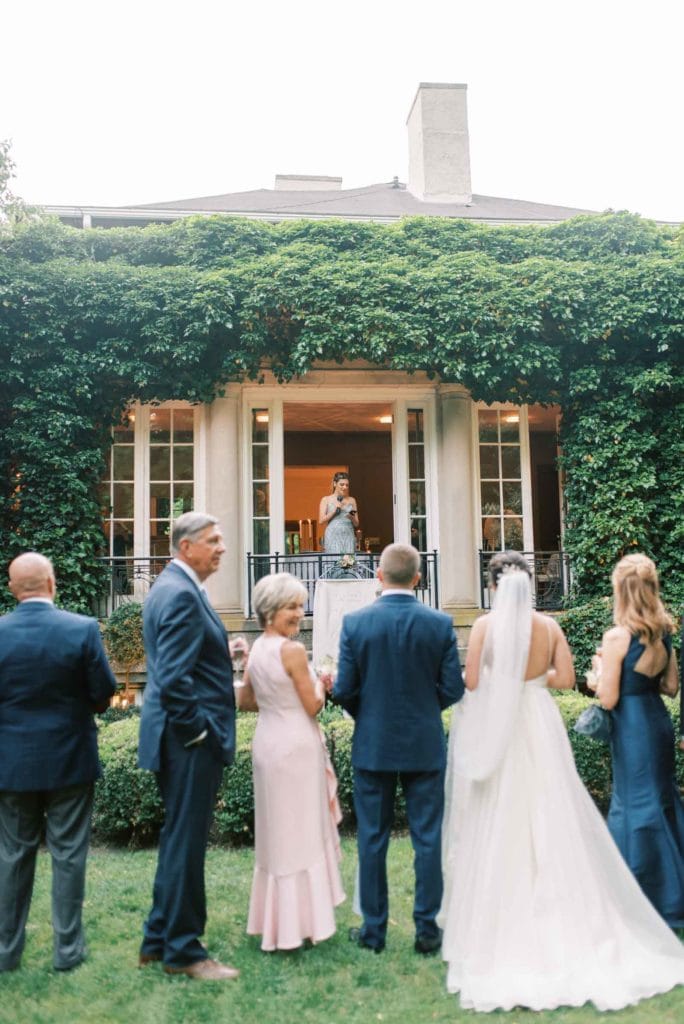 Bridesmaid sharing a speech by the door of the venue with the bride and groom along with the other guests at the lawn, shot by Marcela Diaz Photography
