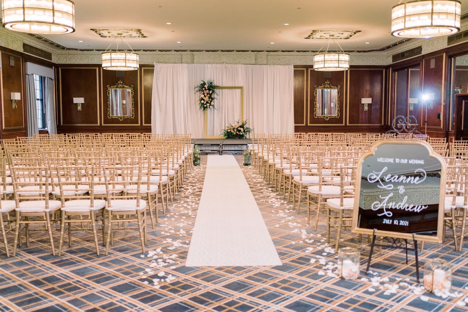 Ceremony space at the Fairmont Copley with a white aisle, white chairs, a wedding arch with white backdrop and a wedding sign that reads Leanne & Andrew