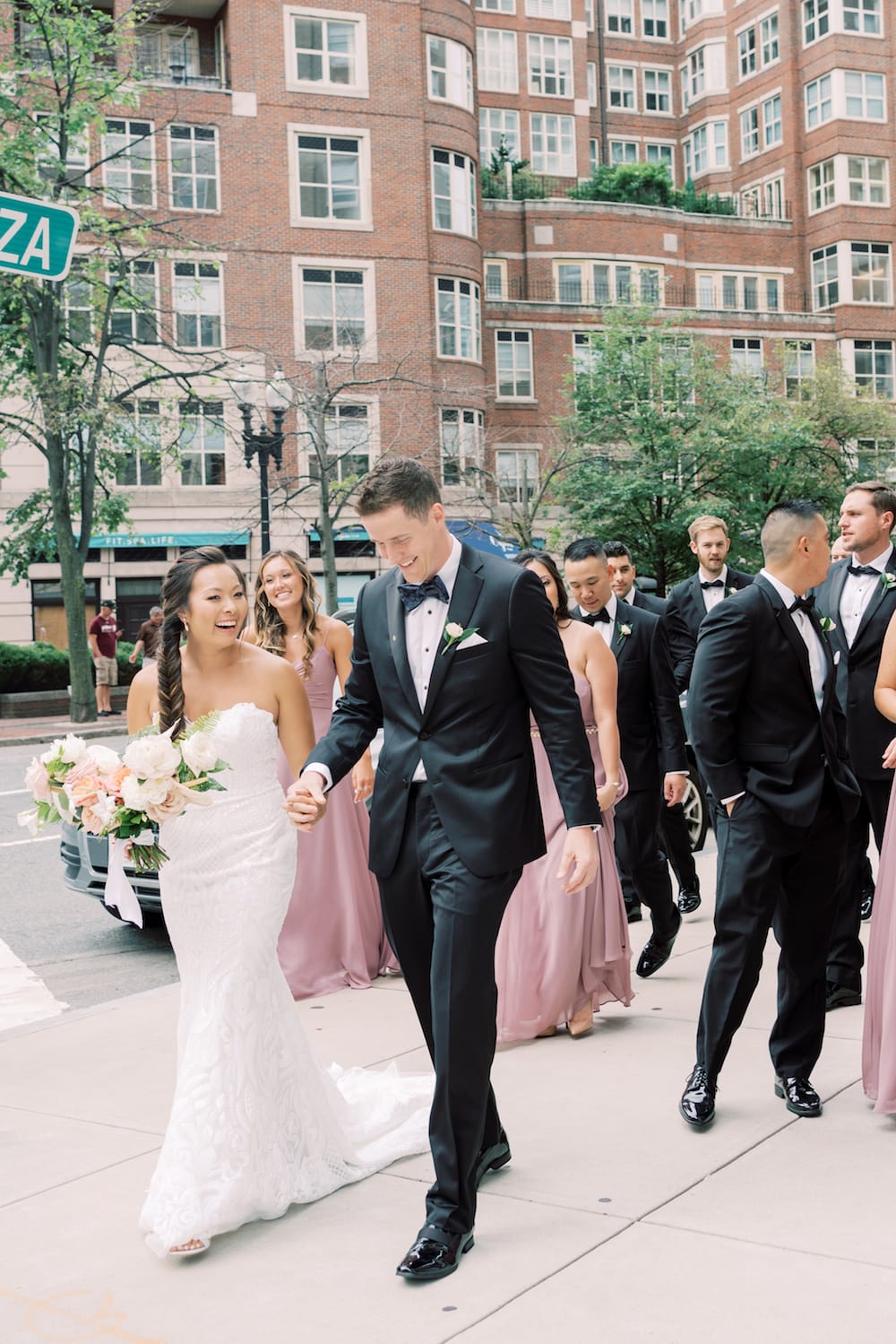 Bride and groom sharing alughs as they walk along Boston with their entourage, taken by Marcela Diaz Photography