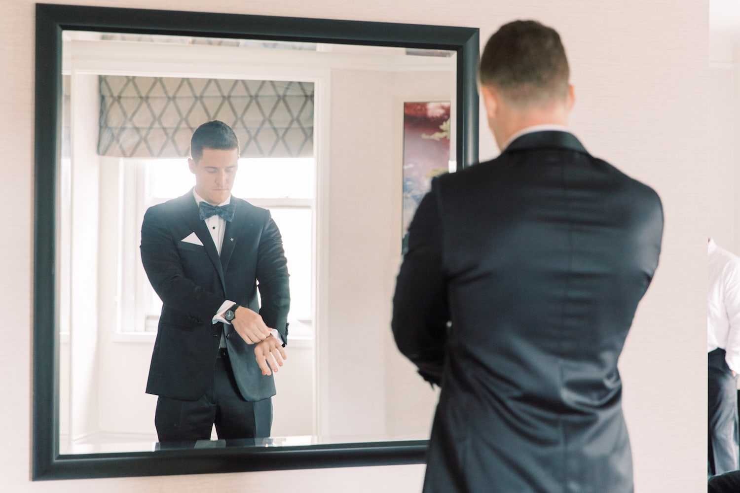 Groom fixing the sleeve of his tuxedo as he stands in front of a mirror in his suite at the Fairmont Copley Plaza