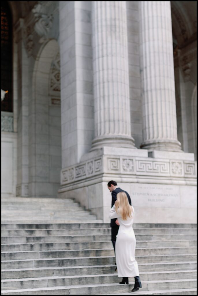 bride in white dress walking up NYC public library stairs with groom.